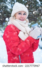 Mature Woman Wearing White Hat Drinks Hot Drink From Travel Mug Enjoying Frosty Weather Closeup. Snowy Winter Forest At Heavy Snowfall