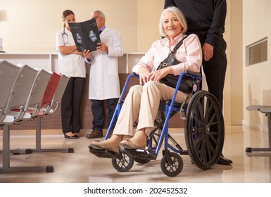 Mature woman in wheelchair in the hospital with her husband. Doctors analyzing scan in background. - Powered by Shutterstock