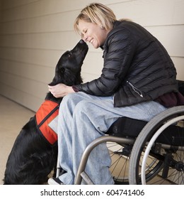 A Mature Woman Wheelchair User With Her Service Dog, A Black Labrador, Leaning In Towards Each Other