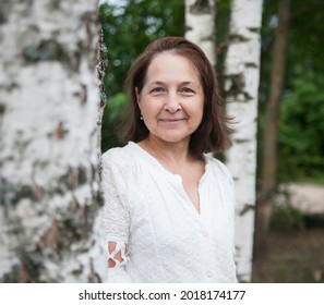 Mature woman in white, with loose hair, against   background of nature. 