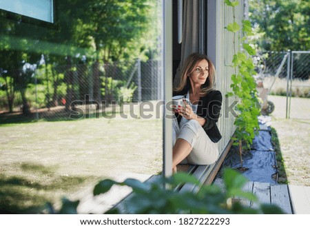 Mature woman working in home office in container house in backyard, resting.