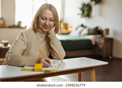 Mature woman writes in her diary sitting at a desk in her room at Christmas home. Thinks about plans, keeps a diary. - Powered by Shutterstock