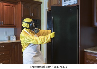 Mature Woman In Yellow Haz Mat Sui And Gas Mask Opening Refrigerator Door In Home Kitchen.