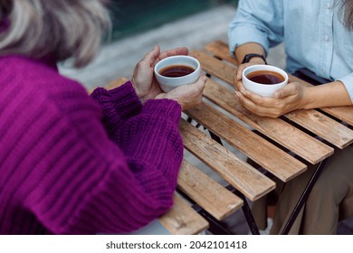 Mature women best friends with cups of fresh coffee sit at wooden table on outdoors cafe terrace on autumn day closeup - Powered by Shutterstock