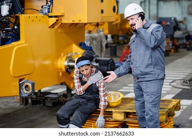 Mature worker of warehouse in workwear calling ambulance for his female colleague with injury or contusion in her shoulder