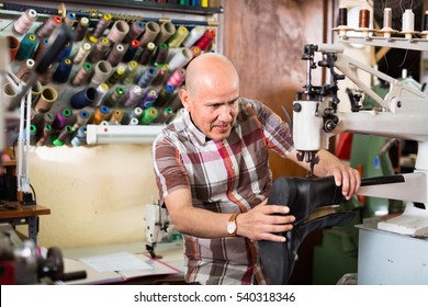 Mature workman sewing leather boots on stitch lathe in workshop - Powered by Shutterstock