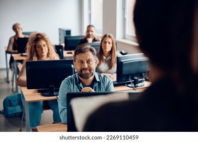 Matures man listening to a teacher while attending computer class in the classroom.  - Powered by Shutterstock