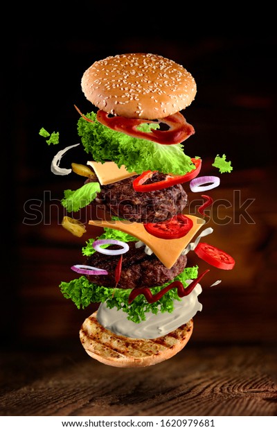 Maxi hamburger,\
double cheeseburger with flying ingredients isolated on wooden\
background. High resolution\
image