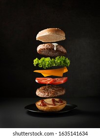 Maxi hamburger with flying ingredients placed on black background. Conceptual jumping Burger. Delicious and attractive hamburger with refreshing ingredients