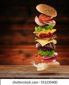 Maxi hamburger with flying ingredients placed on wooden planks. Copy space for text, high resolution image