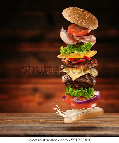 Maxi hamburger with flying ingredients placed on wooden planks. Copy space for text, high resolution image