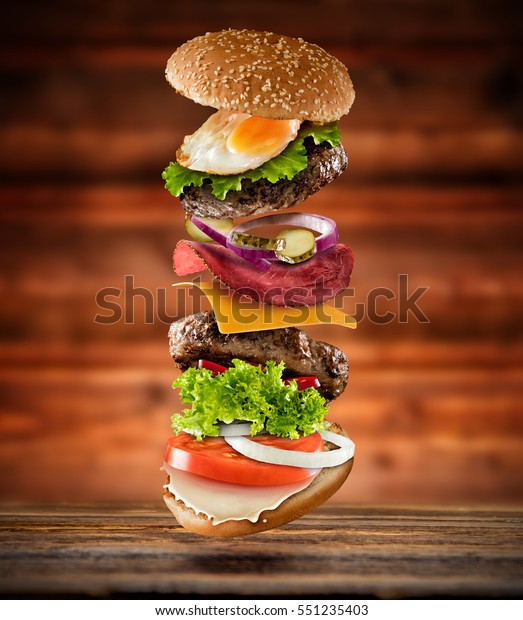 Maxi hamburger with\
flying ingredients placed on wooden planks. Copy space for text,\
high resolution image