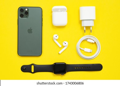 May 01, 2020, Rostov, Russia: Set of Apple devices, black iPhone and AppleWatch, white AirPods with box, power plug, wire Apple lightning to usb type c, arranged in strict lines on yellow background.