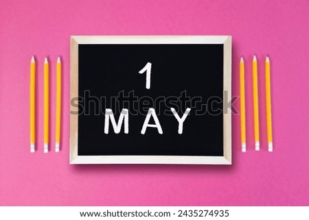 May 1 written in chalk on black board. Calendar date 1st of May on chalkboard on pink blurred school stationery background. Event schedule date. School, study, education concept. Month of spring.