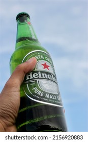 May 14 2022-Chiangmai, Thailand: For Editorial Use Only, Green Color Single Heineken Beer Bottle In South East Asian Male Left Hand With Blur Blue Sky And White Cloud As Background Wiht Empty Space.