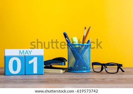 May 1st. Day 1 of month, calendar on business office table, workplace at yellow background. Spring time
