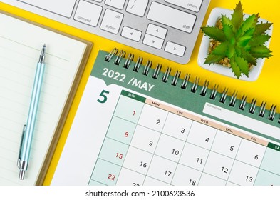 May 2022 desk calendar and diary with keyboard computer on yellow background.
