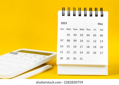 May 2023 Monthly desk calendar for 2023 year and calculator with pen on yellow background.