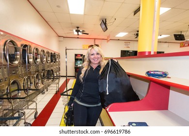 MAY 7 2016 - SAN DIEGO, CALIFORNIA: A Blonde Female Does Her Laundry In A San Diego Laundromat, Holding Her Black Laundry Bag. 