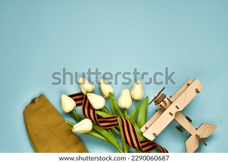 May 9. St.George ribbon, wooden plane,military cap, white tulips on a blue background. The traditional symbol of Victory Day 1945. Victory Day holiday. Banner. Postcard. Flat lay, copy space 