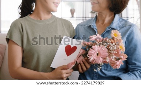 May Mother's day young adult grown up child cuddle hug give flower gift box red heart card to mature middle aged mum. Love kiss care mom asia people sitting at home sofa happy smile enjoy family time.