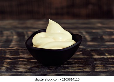 Mayonnaise in a black bowl. Homemade mayonnaise on a black old table. Black bowl with sauce on a background of dark wooden boards.