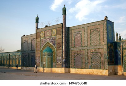 Mazar-i-Sharif, Balkh Province In Afghanistan. Two Men Walk Past The Blue Mosque In Mazar I Sharif In The Sunshine. Colorful Mosaics And Tiles Adorn The Mosque Walls. Northern Afghanistan.