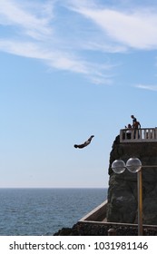 Mazatlan/MX: March 16, 2017 – Cliff Diver, Also Known As El Clavadista, On The Malecon Swan Dives From 50 Foot High Platform Into Water That Is Five Feet Deep. Tourists With Cameras On Platform Watch.