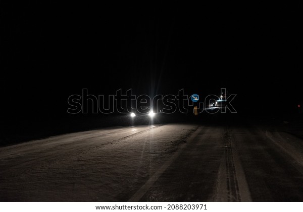 Mazowieckie, Poland - December 5, 2021: Night photo\
of road traffic in winter. Car lights reflecting off an icy,\
slippery road.