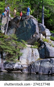 MCCRAE LAKE, ONTARIO - AUG 19: Group Of Children Standing On Top Of A Cliff And Jumping Several Meters Deep Into McCrae Lake Below. Photographed From A Boat On Aug 19, 2009.