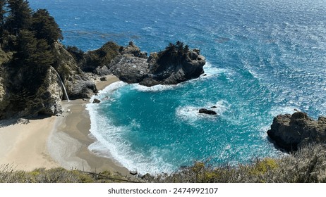 McWay Falls cascading onto a sandy beach in a small, secluded cove with turquoise waters. Lush green cliffs surround the area, and the ocean extends into the horizon under a clear sky. - Powered by Shutterstock