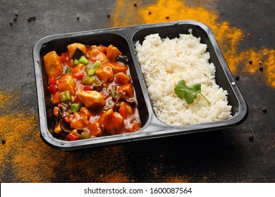 A Meal In A Box. Chinese Style Chicken With White Rice. Ready Dish In A Black Container. Composed Take-out Meal, Diet Catering. The Container On A Dark Background.