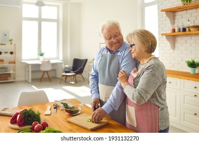 A Meal Cooked With Love Tastes Better. Happy Senior Couple Cooking Healthy Lunch Together In Kitchen Of Their Modern Studio Apartment. Smiling Mature Husband Helping His Wife Chop Vegetables For Salad