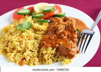 A Meal Of Kashmiri Lamb Curry With Rice And Salad On A Maroon Tablecloth.