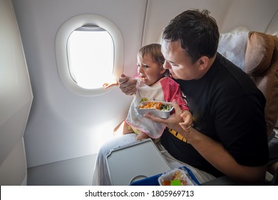 Meal Onboard Of Aircrafl Economy Class. Father Feeds The Little Toddler On The Plane With Special Meals.