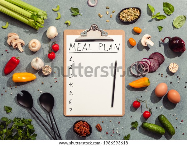 Meal\
plan concept. Food ingredients, salad serving utensils and\
clipboard with letters MEAL PLAN and seven numbers. Gray\
background. Diet menu concept. Top view, flat\
lay