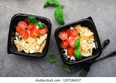 Meal Prep. Delicious Homemade Dinner Pasta Bows, Cherry Tomatoes, Granulated Curd, Basil In Black Plastic Containers On A Dark Background With Black Forks. Top View.