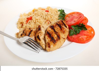 A Meal Of Spicy Grilled Cajun Chicken Breasts With Vegetable Rice And Fresh Tomato