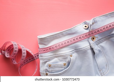 Measure tape with light blue jeans on the pastel pink background. Women diet. Mock up for healthy lifestyle, body slimming, weight loss or dressmaker's offer or other ideas. Empty place for text.