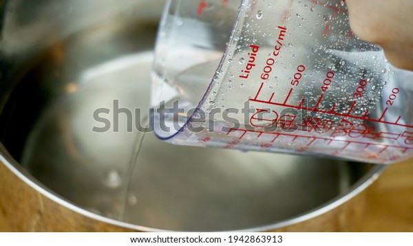 Measurement cup or measurement\
jug is usually used to measure liquid ingredients like water, milk,\
oil. \
\
In frame measurement cup pouring water into a\
pan
