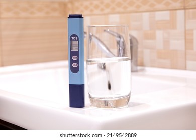 Measurement Of TDS Of Water. Electronic PH Meter In A Glass Of Water. In The Background Is A Tap For Drinking Water. Cleaning The Water In The Bathroom.