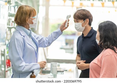 Measures To Prevent People With Fever,Covid 19 Concept. Elderly Female Pharmacist Uses A Digital Thermometer To Measure The Temperature Asian Male And Female Customer And Wears A Mask In Pharmacy.