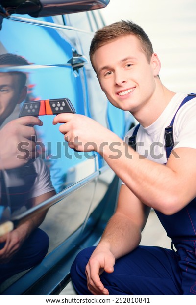 Measuring coating thickness. Closeup of a\
handsome car mechanic checking the thickness of car coating with a\
special electronic tool in car repair\
station