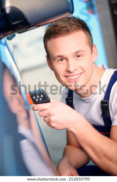 Measuring coating thickness. Top view of a\
handsome car mechanic examining the car coating with a special\
electronic device in car service\
station
