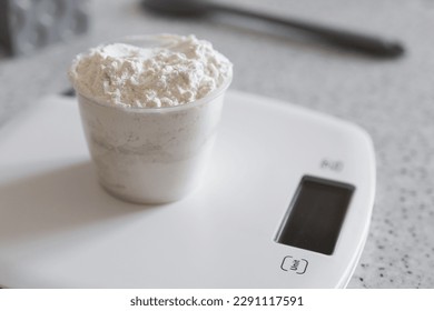 Measuring cup with flour on a white kitchen scale.