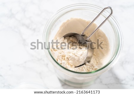 Measuring cup inside glass jar filled with all-purpose flour.
