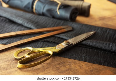 Measuring and cutting textile or fine cloth. Work table of a tailor. Gold scissors and black fabric. 