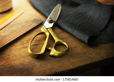 Measuring and cutting textile or fine cloth. Work table of a tailor. Gold scissors and black fabric. 