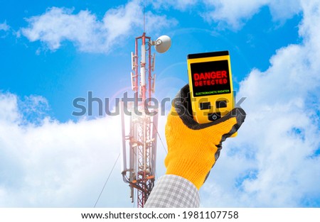 Measuring electromagnetic radiation from a cell tower. The device indicates hazardous radiation with text Danger. Influence of the electromagnetic field on humans concept.