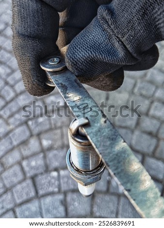 Measuring the spark plug gap using a feeler gauge for optimal combustion is done by wearing gloves for the comfort of the mechanic working.